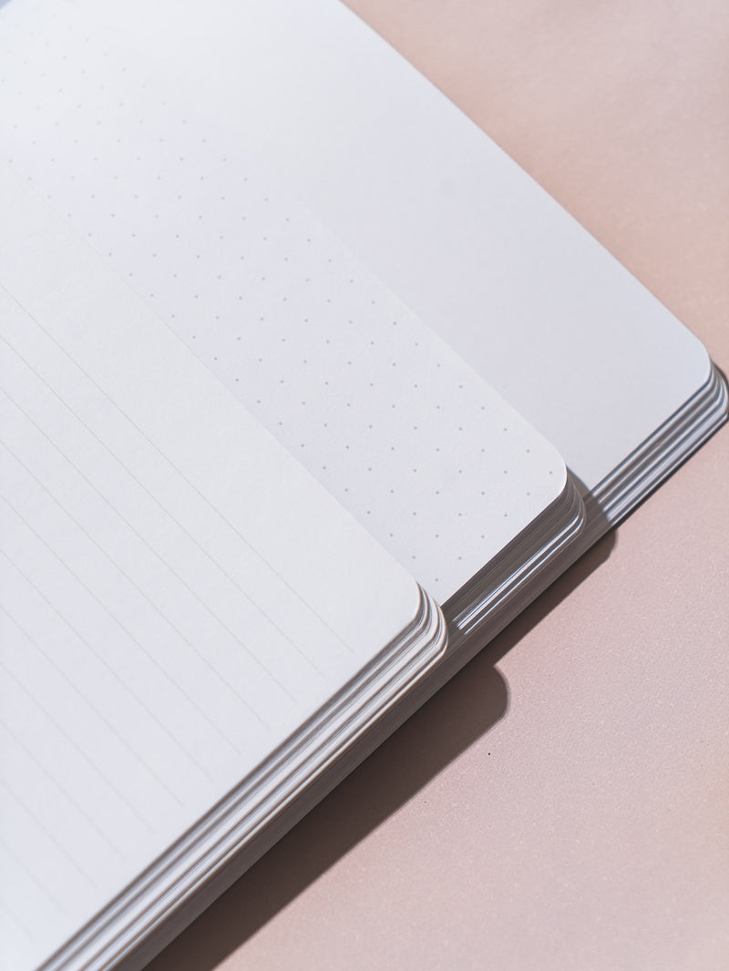 close-up of corners of three pastel notebooks overlapping on pink surface, open to show paper types: blank, lined, dotted