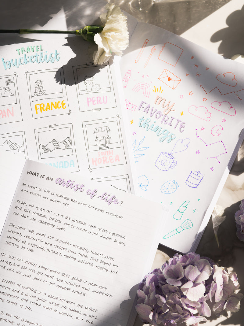 three pastel notebooks open featuring colorful doodles and writing, next to white and purple flowers