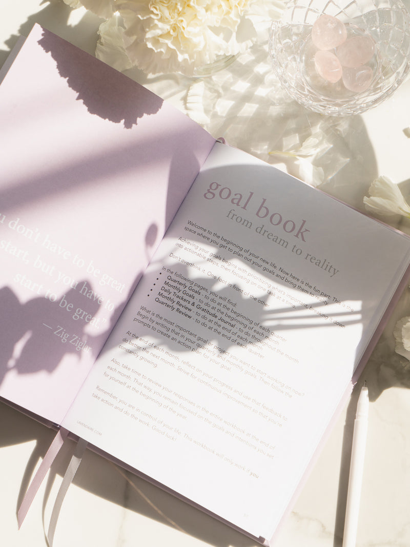 lavender artist of life workbook open to goal book section, next to white flowers and bowl of pink crystals