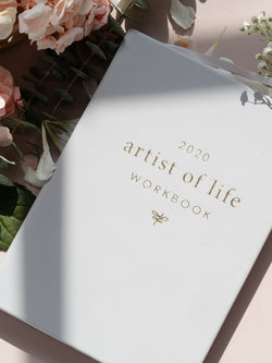 Lavendaire Grey Artist of Life Workbook next to pink and white flowers