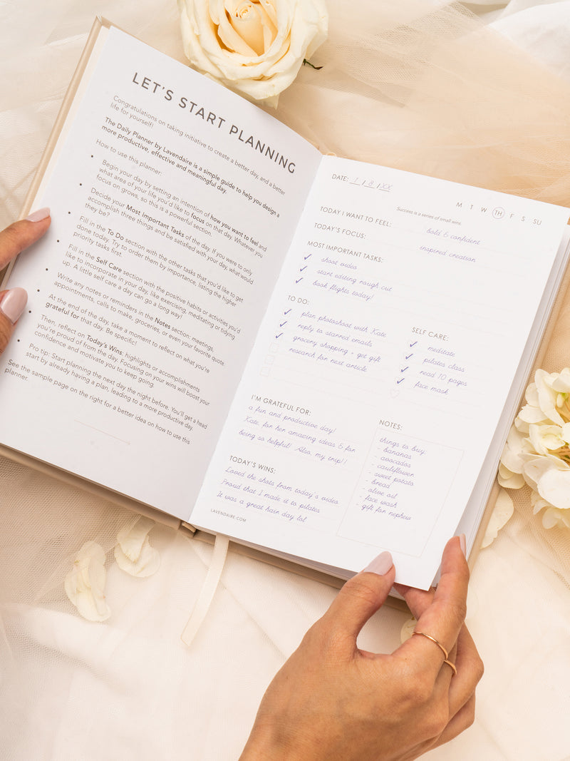 Hands open Lavendaire Daily Planner to instruction pages on tulle surrounded by flowers