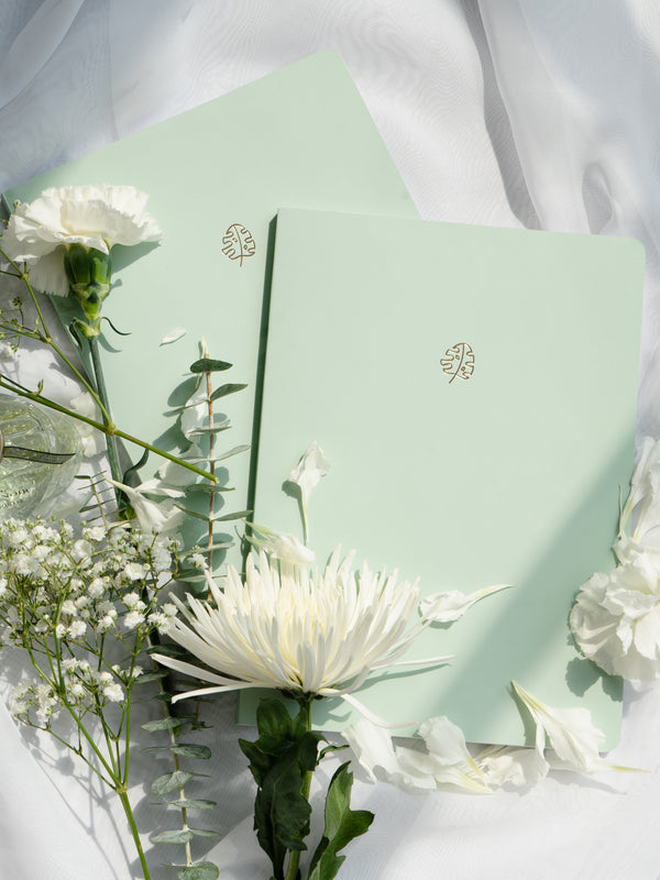 two green pastel notebooks on white fabric background surrounded by white flowers
