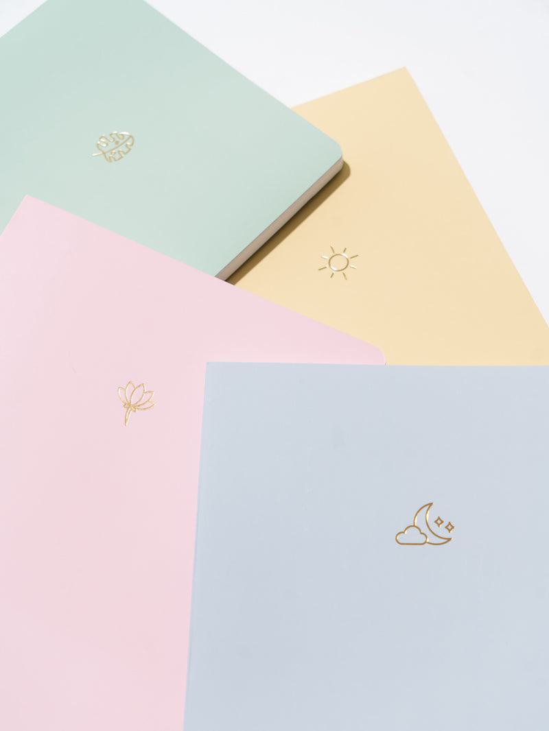 blue, pink, green, and yellow pastel notebooks stacked unevenly on each other, on white surface